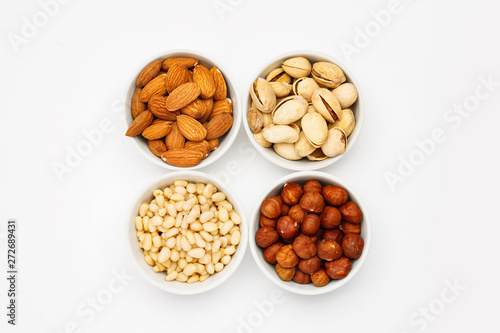 Different nuts in ceramic bowls on a white table, top viev