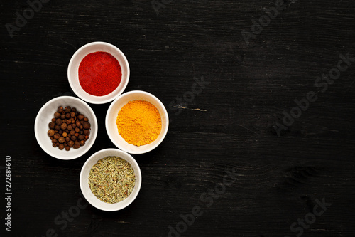 Different spices in ceramic bowls on a black wooden table, top view, text space