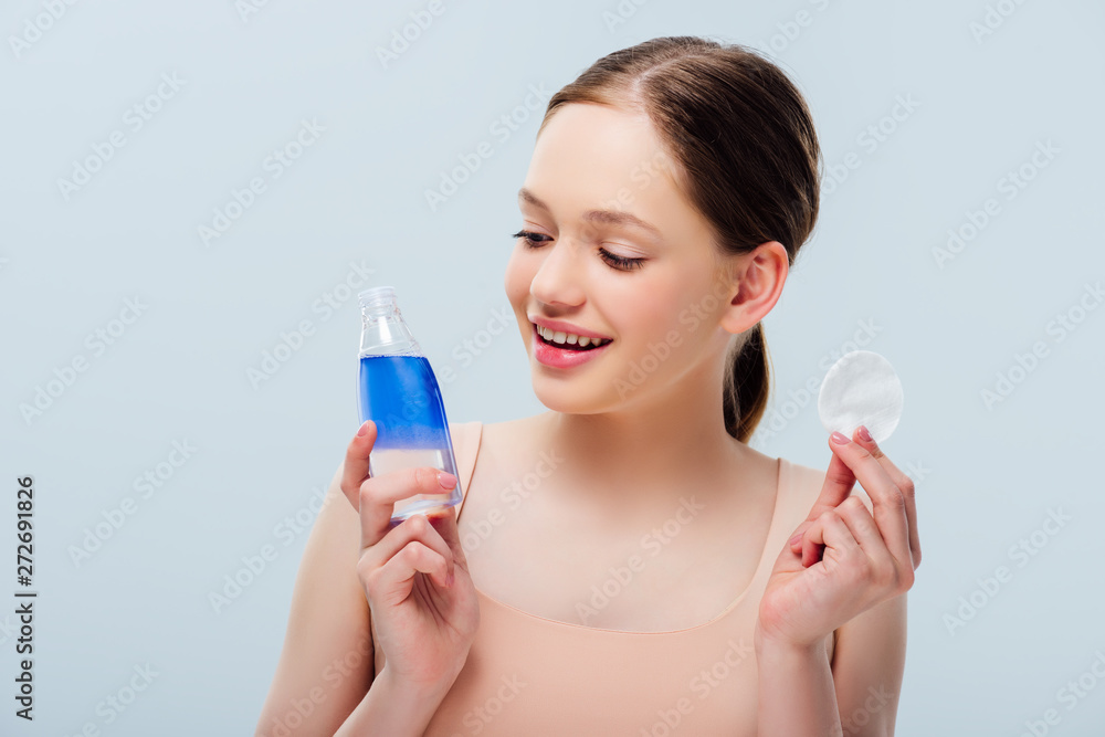 pretty teenage girl holding blue lotion and cotton pad isolated on grey pretty teenage girl holding blue lotion and cotton pad isolated on grey
