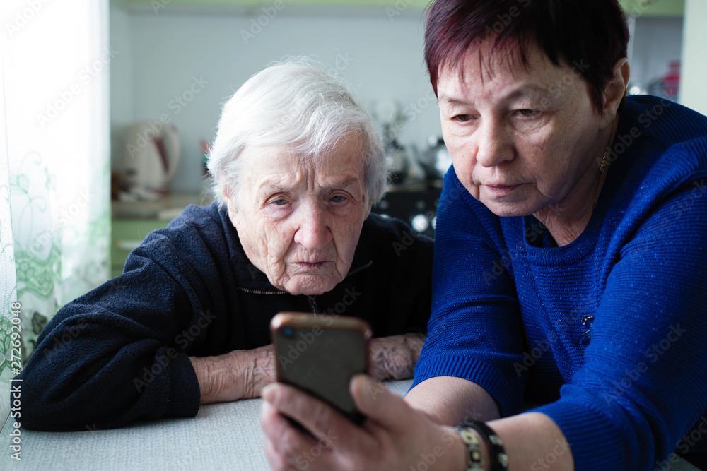 An adult woman shows an old woman the smartphone screen. An adult woman shows an old woman the smartphone screen.