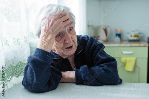 Frustrated gray-haired old woman sitting at home at the table.