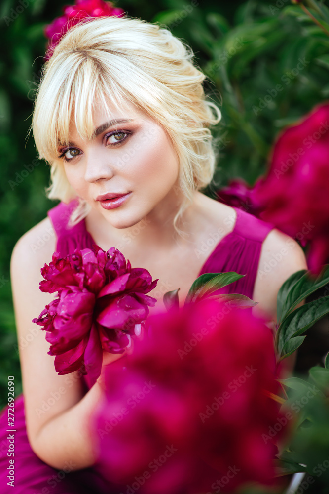 Naklejka premium Outdoor close up portrait of beautiful young woman with long blonde hair, makeup, posing in the blooming garden. Female spring fashion concept
