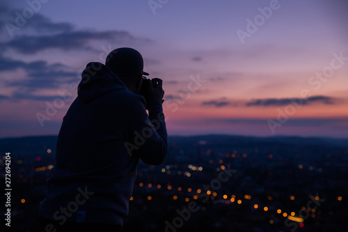 Photographer taking photos of colorful sunset on Bila Hora with amazing view on city Brno Czech Republic pink and orange colors with many clouds and city lights © Lukas