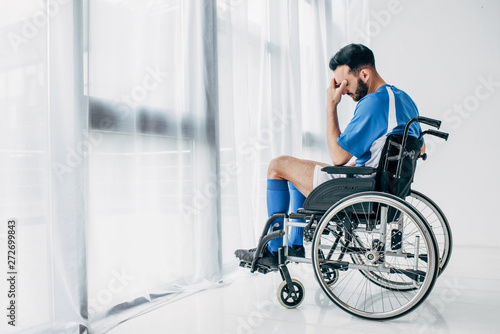 upset man in football uniform sitting in Wheelchair in hospital near window