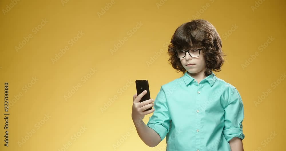 Little cheerful boy using his smartphone when suddenly getting surprised and happily smiling, isolated on yellow background - emotions concept close up 4k Little cheerful boy using his smartphone when suddenly getting surprised and happily smiling, isolated on yellow background - emotions concept close up 4k
