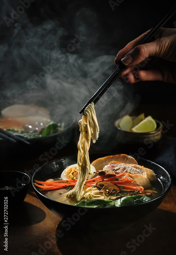 Hand with chopsticks takes noodles of ramen soup. Traditional Asian cuisine
