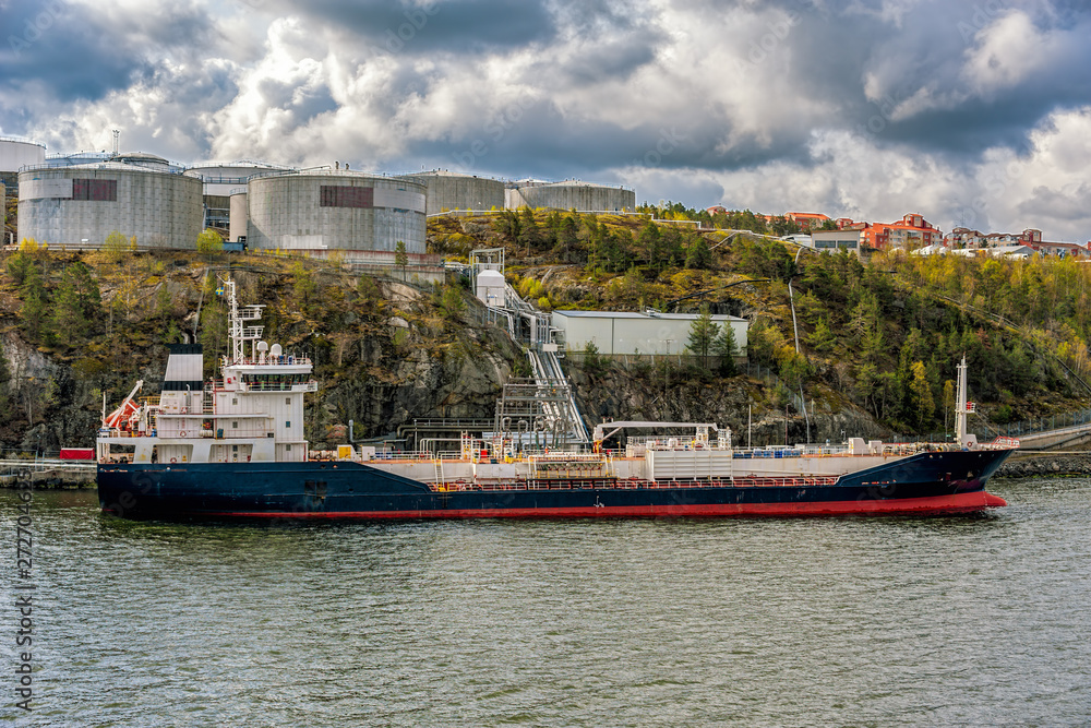 Oil/Chemical tanker sit berthed at a shore terminal with a oil product storage tanks above on Stockholm archipelago coast.