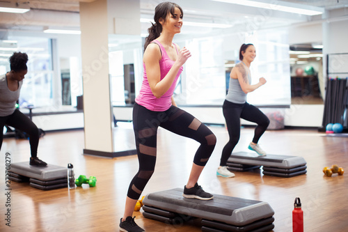 Tableau sur toile Smiling confident female athletes exercising on aerobics steps in gym