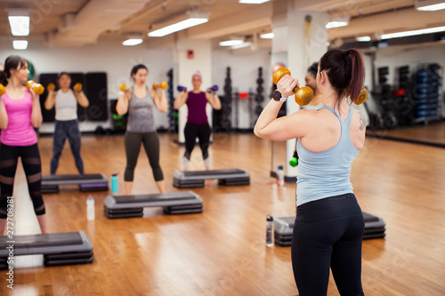 Photography Rear view of trainer with dumbbells instructing athletes in gym