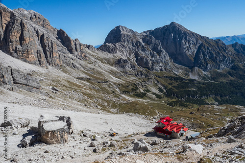 Tourist with hiking backpacks in mountain hike on summer day. Man traveler hiking in beautiful mountain landscape. Climber and alpine hut Silvio Agostini in Dolomites Alps, Italy. © Lubos Chlubny