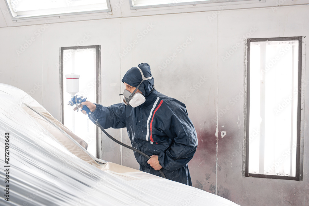 Car service station. Worker painting a white car in special garage, wearing costume and protective gear Car service station. Worker painting a white car in special garage, wearing costume and protective gear
