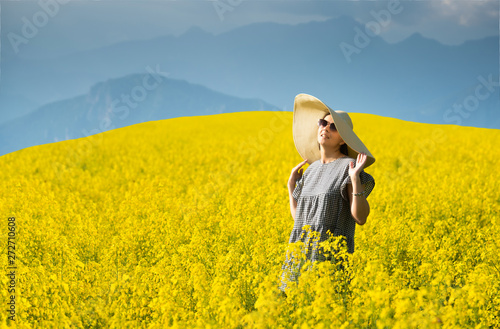 Smiling pretty girl  in blooming yellow field with mountains on background.