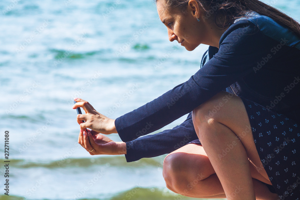 Woman on the beach taking pictures on a smartphone on the background of the surf