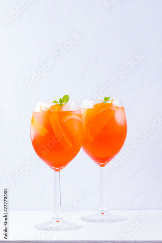 Aperol Spritz cocktail with mint leaves on a white background. A glass of summer alcohol cocktail with orange slices. Classic Italian drink coral color