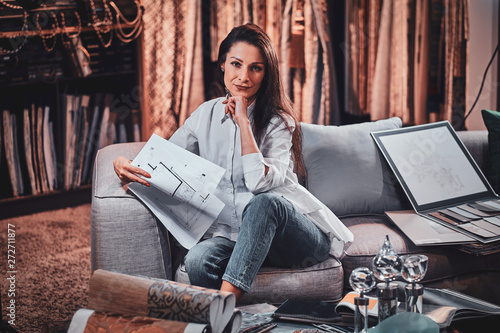 Attractive pensive woman is sitting on the sofa at her curtians atelier while handing drawings about her new project. photo