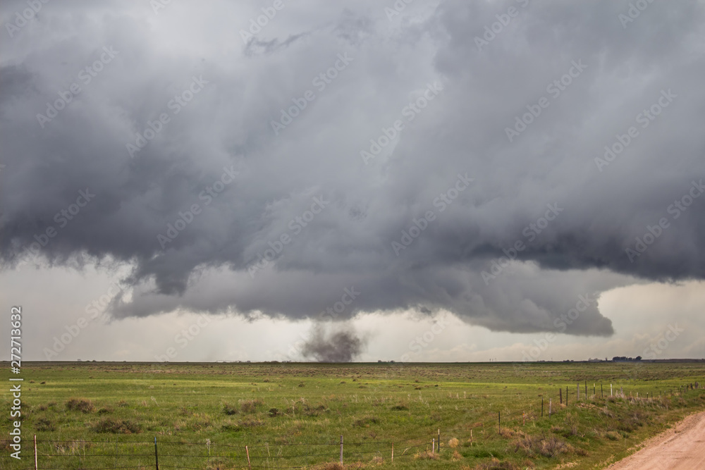 A tornado with no visible funnel touches down on the plains and swirls dust beneath a storm.