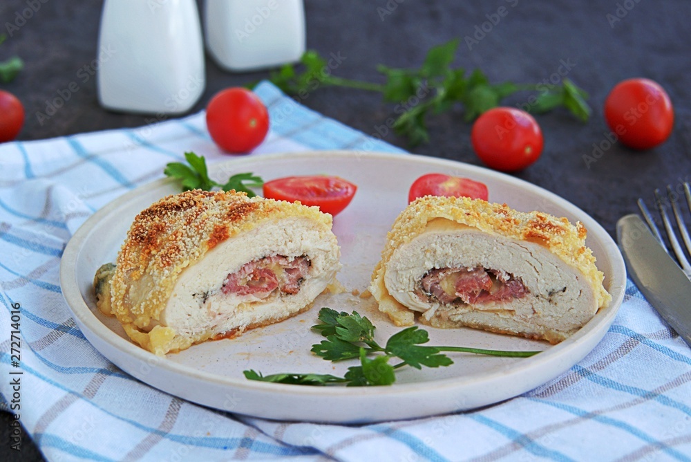 Homemade fillet Cordon Bleu or chicken fillet with ham and cheese on a white clay plate on a dark brown background. Swiss cuisine. Selective focus. Homemade fillet Cordon Bleu or chicken fillet with ham and cheese on a white clay plate on a dark brown background. Swiss cuisine. Selective focus.