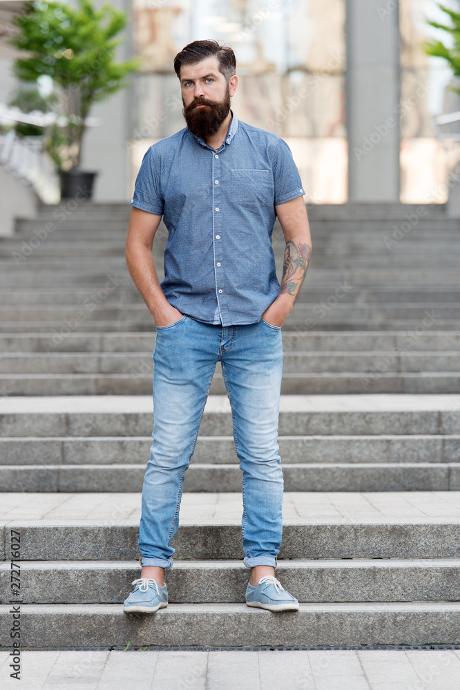In love with denim. Man bearded hipster fashion model wear denim clothes  urban background stairs. Regular walk in city center. Confident guy wear  jeans denim trousers and shirt. Comfortable outfit Stock Photo