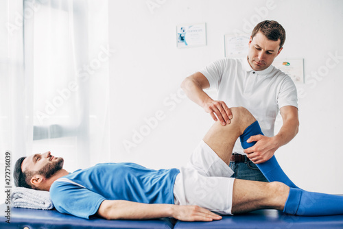 Fototapeta Naklejka Na Ścianę i Meble -  handsome Physiotherapist massaging leg of football player in hospital