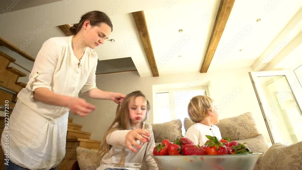 Daughter eats strawberry while mother comb hair and brother. Dish of berries Daughter eats strawberry while mother comb hair and brother. Dish of berries