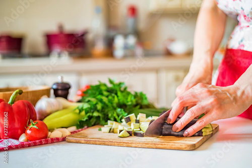 Close up female hand with knife cuts eggplant on wooden board in kitchen