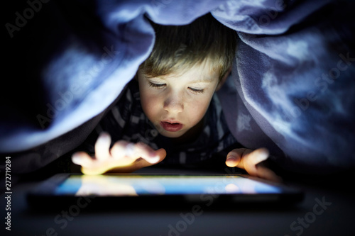 Little boy playing secretly with his digital tablet, hidden under blanket photo