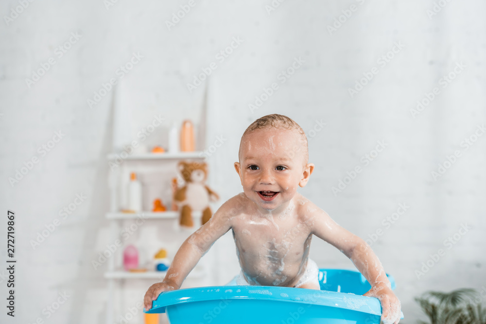 toddler kid taking bath and smiling in blue plastic baby bathtub at home toddler kid taking bath and smiling in blue plastic baby bathtub at home