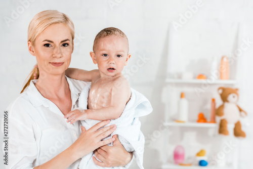 attractive blonde mother holding in arms wet toddler son in bathroom