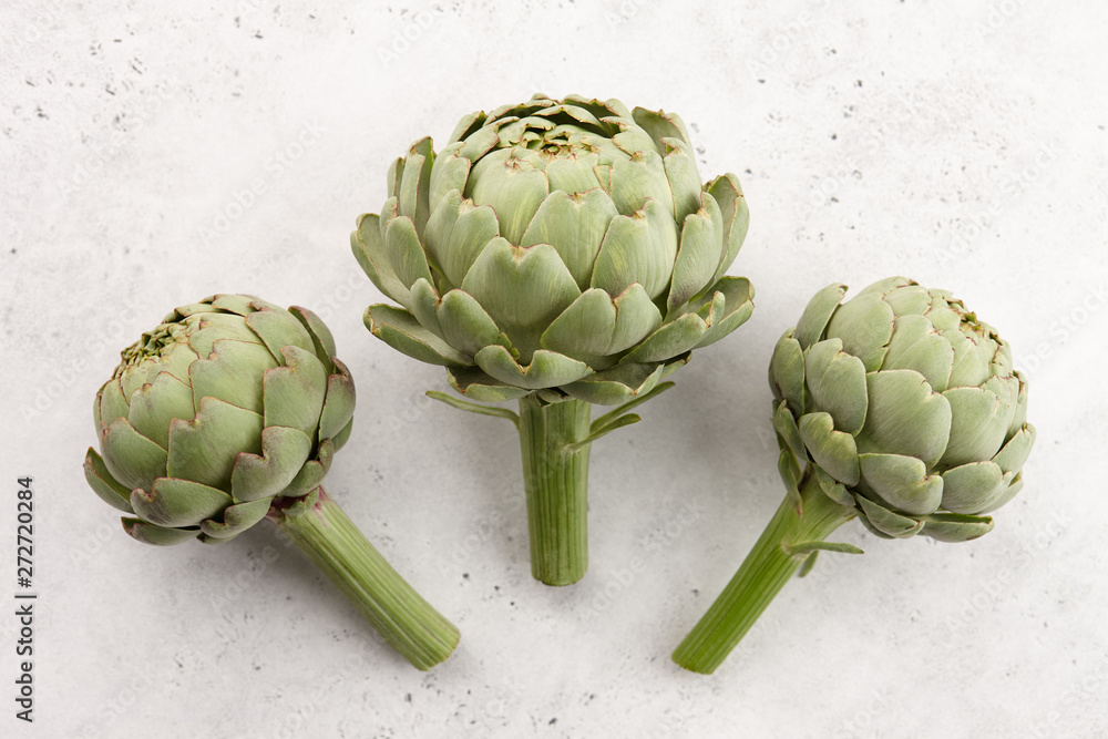 Obraz premium Fresh green artichokes on white stone background, top view