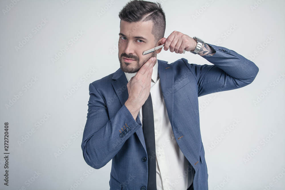 Barbershop advertising concept. Businessman with serious face isolated on white background. Man with beard holds razor. Macho in formal suit shaves beard and moustache. Barbershop advertising concept. Businessman with serious face isolated on white background. Man with beard holds razor. Macho in formal suit shaves beard and moustache.