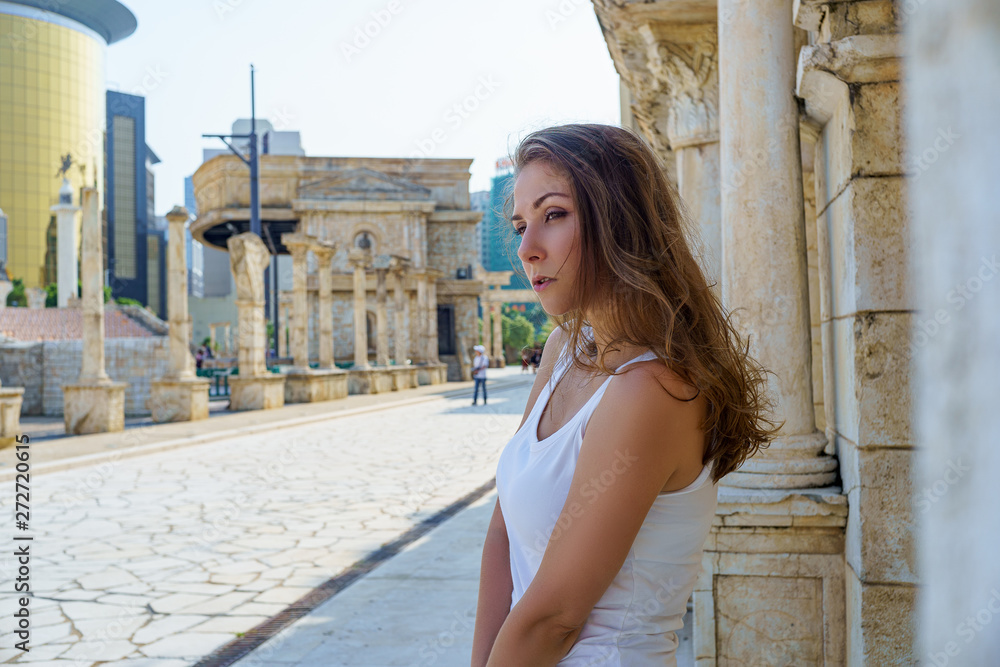 Beautiful girl with brown hair in white dress tender poses on the street in ancient ruins with columns in Rome