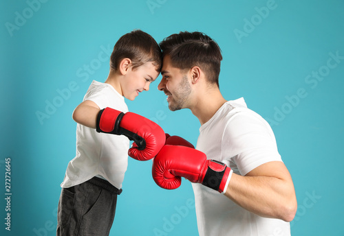 Dad and his son with boxing gloves on color background © New Africa