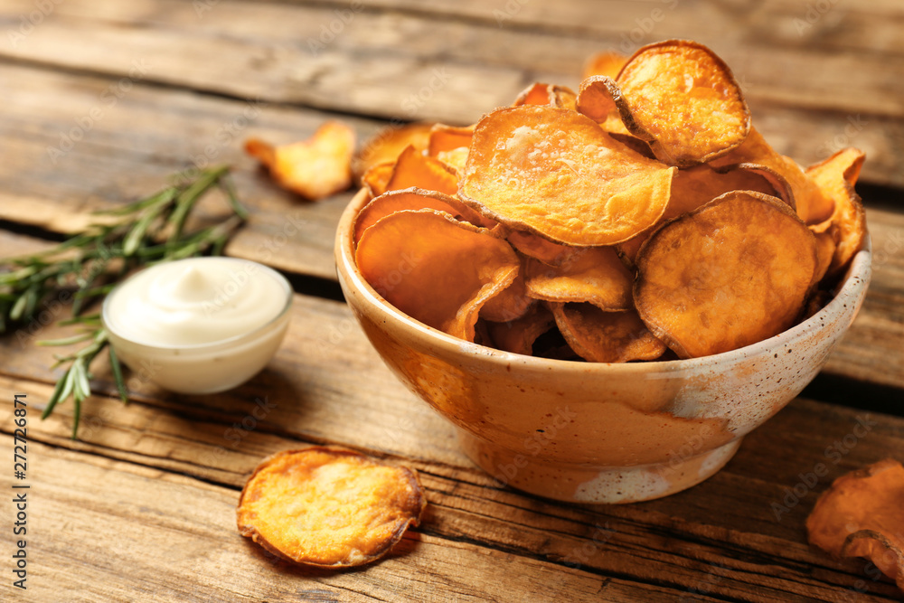 Delicious sweet potato chips in bowl, rosemary and sauce on table. Space for text