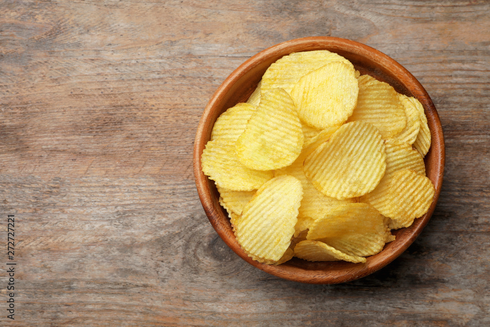 Delicious crispy potato chips in bowl on table, top view with space for text