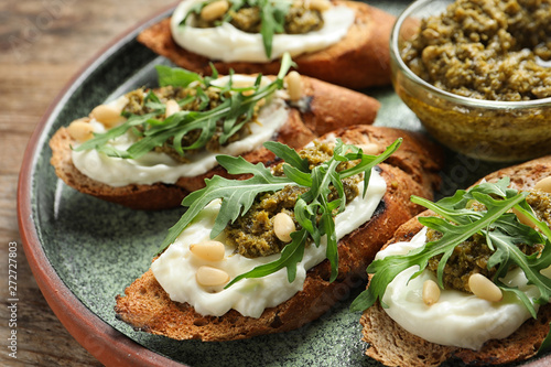 Plate with tasty bruschettas and pesto sauce on wooden table, closeup