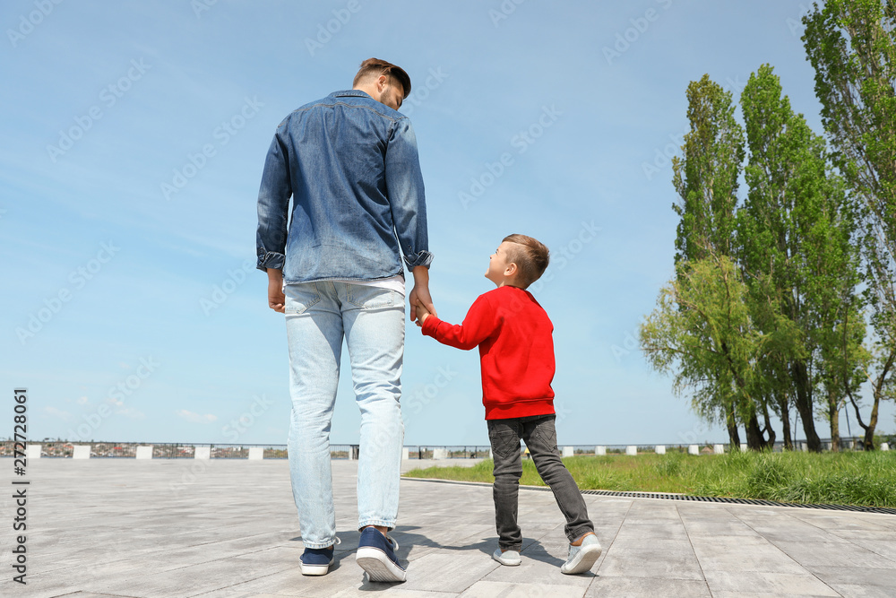 Little child holding hands with his father outdoors. Family weekend