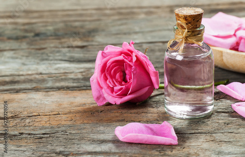 pink rose flower and glass of bottle essential oil or rose water with rose petals, spa and aromatherapy cosmetic concept