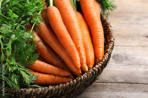 Basket of carrots on wooden background, closeup photo