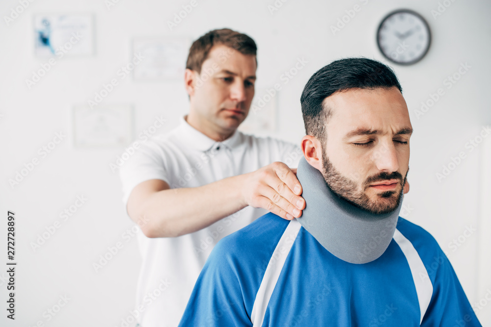 chiropractor examining good-looking football player in neck brace in hospital chiropractor examining good-looking football player in neck brace in hospital