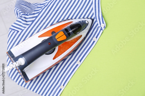 Modern electric iron and shirt on color background, top view with space for text. Laundry day