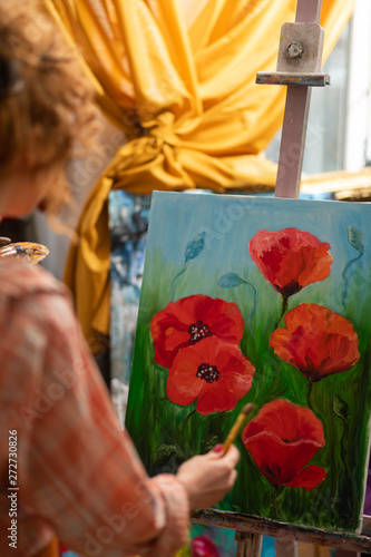 Curly red-haired artist standing near canvas with red poppies