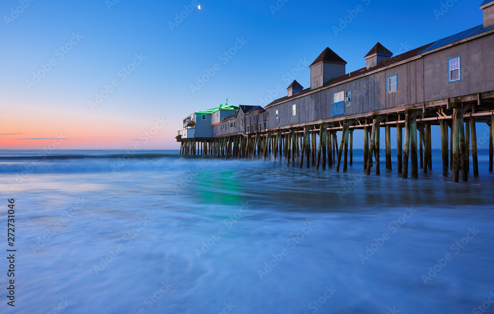 The Pier at Old Orchard Beach of Maine before sunrise. The wooden pier on the beach contains many other tourist businesses, including a variety of souvenir shops.