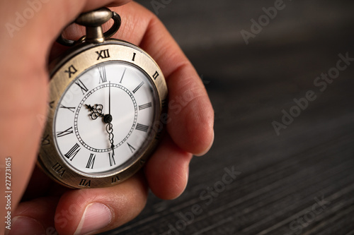 Men hands hold a pocket watch and a black background.