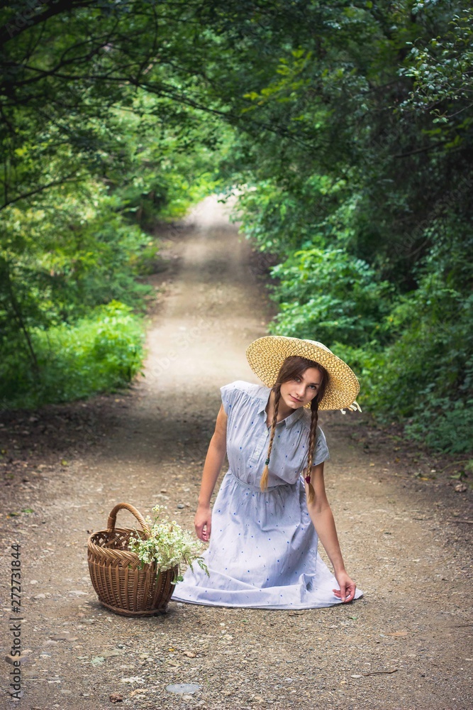 Obraz premium Girl in blue floral with yellow hat dress sitting in the middle of the road
