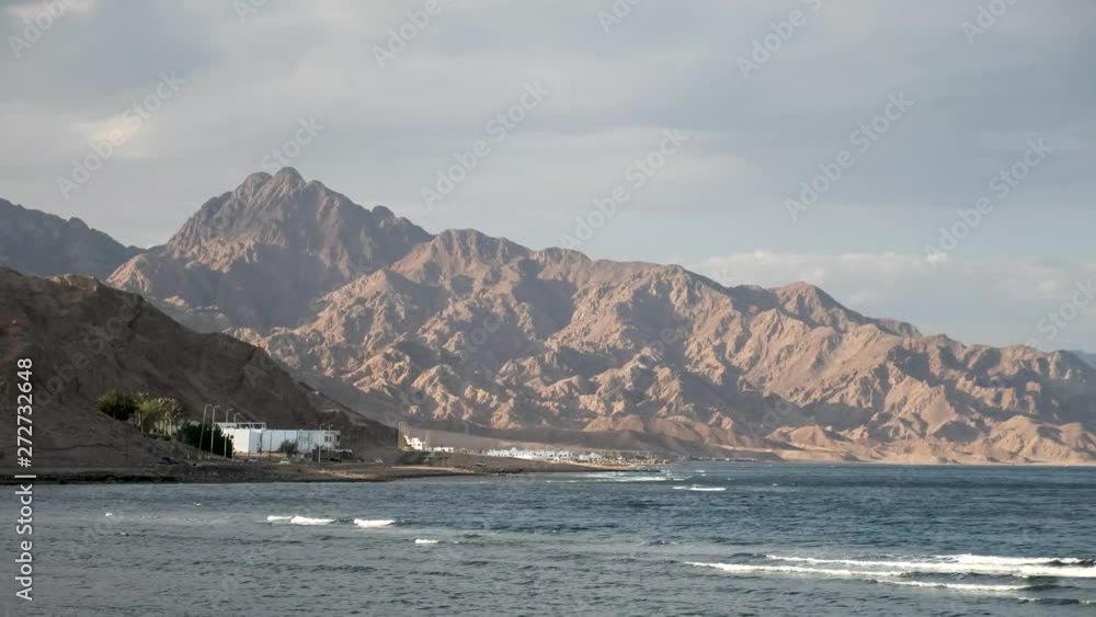 Beautiful clear water in Dahab Egypt. Exploring the blue water with mountains in the background and people windsurfing and kite surfing. Lady walking on the beach Beautiful clear water in Dahab Egypt. Exploring the blue water with mountains in the background and people windsurfing and kite surfing. Lady walking on the beach