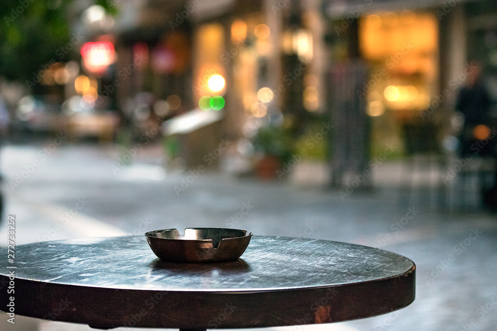 Obraz premium A bar round wooden table with an ashtray, outdoors in the evening, copy space.