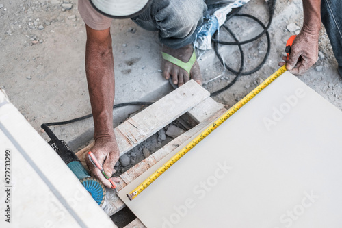 Top view of worker measuring ceramic tile using measure tape and marker prepare for installing at construction site for new house building