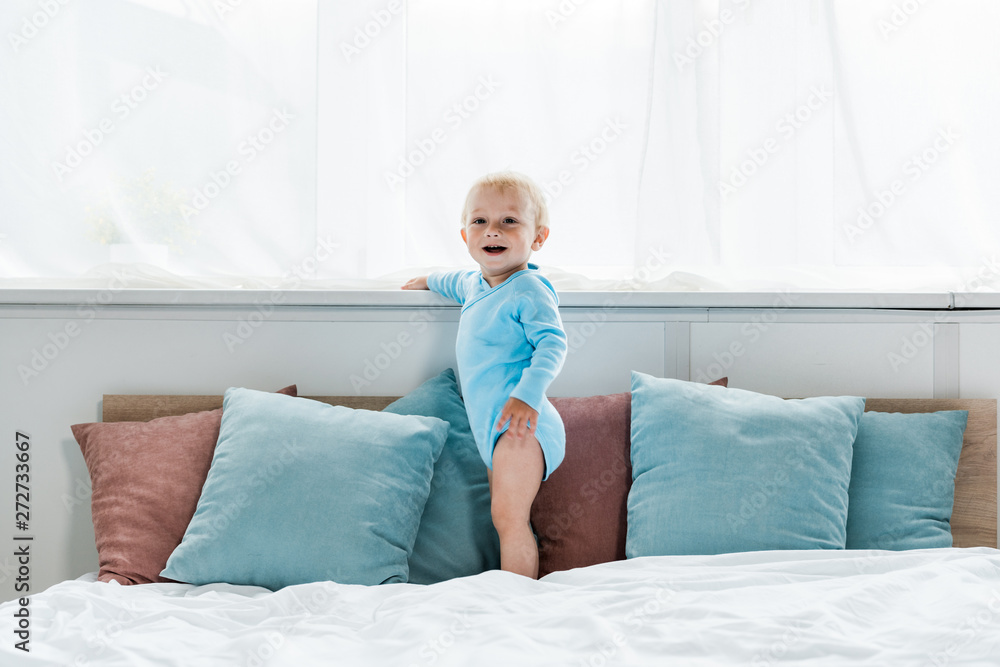 happy toddler kid standing on bed and smiling in bedroom happy toddler kid standing on bed and smiling in bedroom