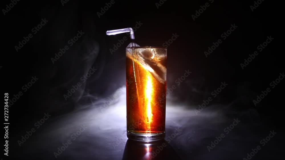 Cocktail glass splashing on dark toned smoky background or colorful cocktail in glass. Party club entertainment. Mixed light. Selective focus Cocktail glass splashing on dark toned smoky background or colorful cocktail in glass. Party club entertainment. Mixed light. Selective focus