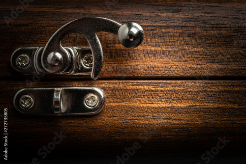 An elegant metal sliding clasp lock screwed into the lid of a wooden box.